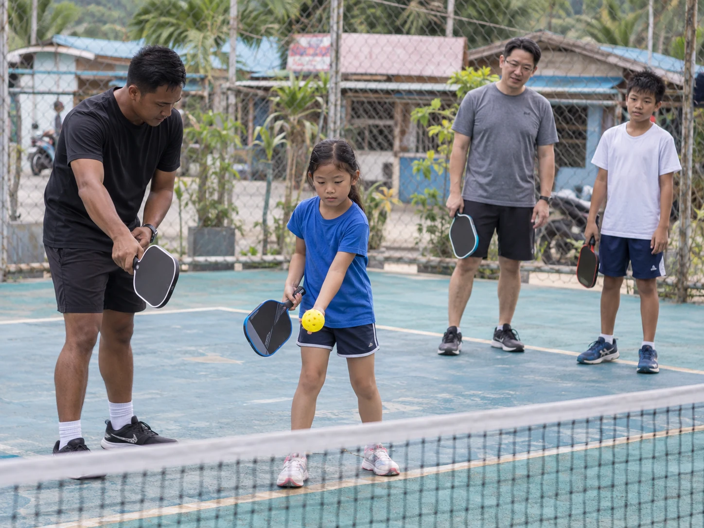 Illustration of two children and a parent learning pickleball with a coach.