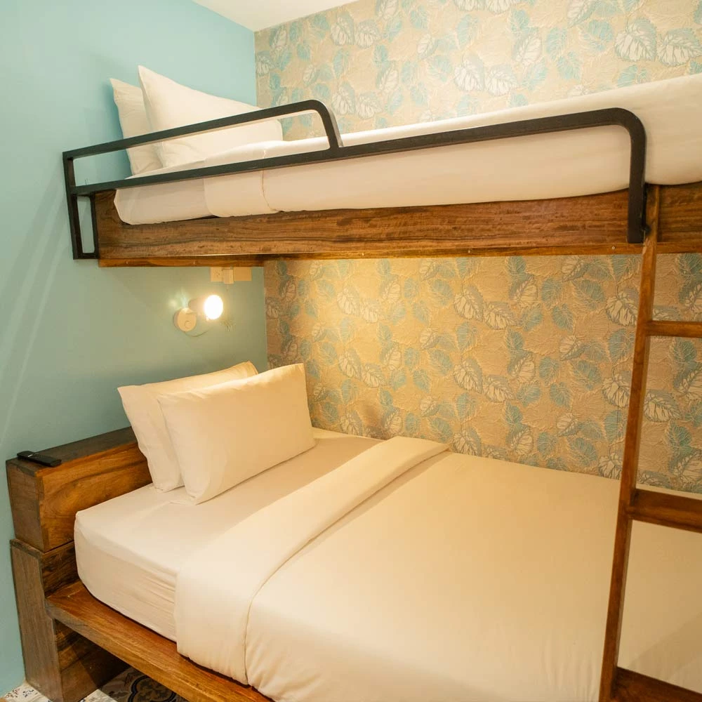 Double Room · Bunk bed with a wide lower bed in white linen, a black rail along the upper bed and leaf-pattern wallpaper · Photo 1 of 3