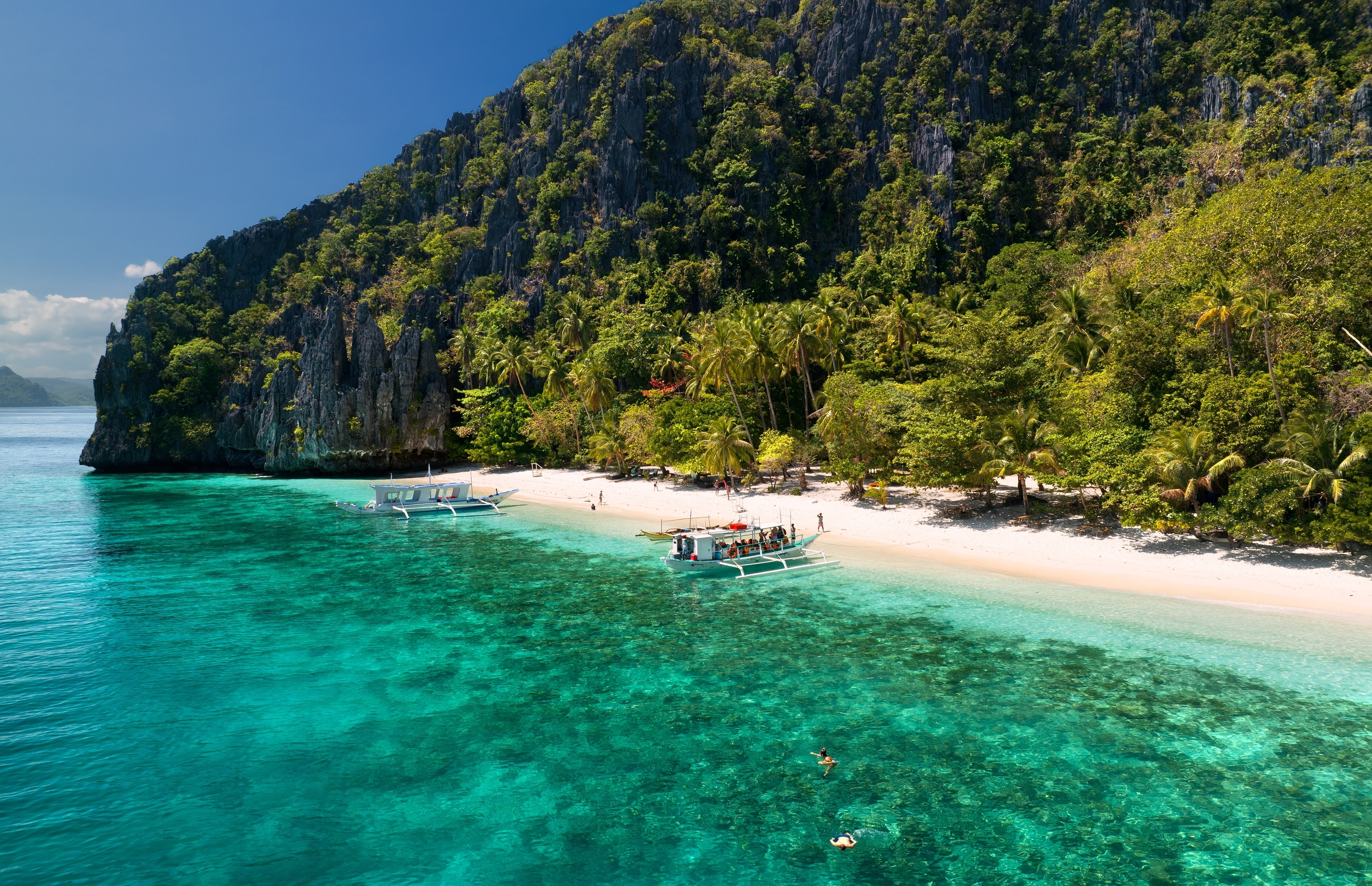White sand beach, turquoise water and boats beside limestone cliffs