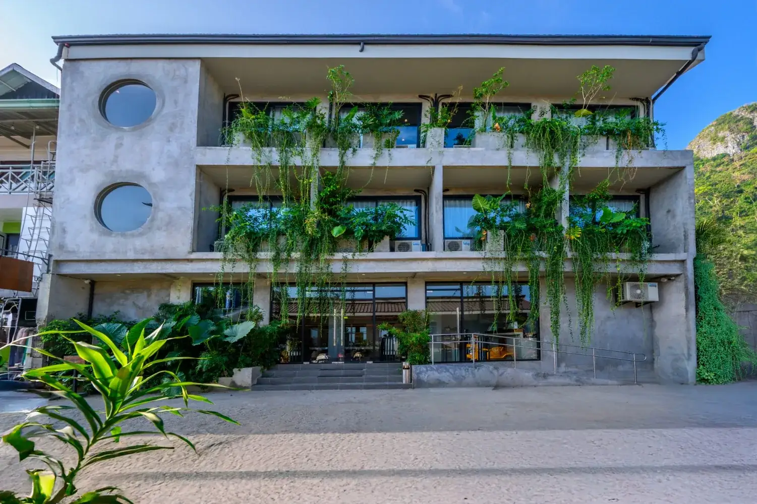 Z Garden Hotel 三層樓清水模外觀，有圓窗，陽台垂掛綠色植物